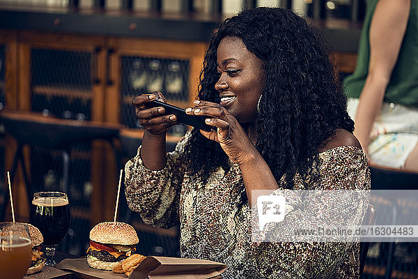 Lächelnde Frau mit Smartphone beim Burgeressen in einer Kneipe