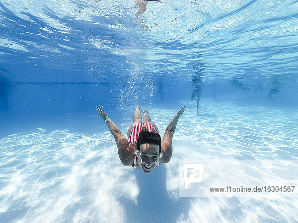 Lächelnde Frau schwimmt unter Wasser in einem Pool in einer Ferienanlage