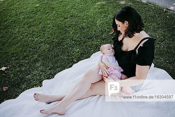 Frau schaut auf süße Baby-Mädchen schlafen auf ihrem Schoß  während sie in Hinterhof sitzt