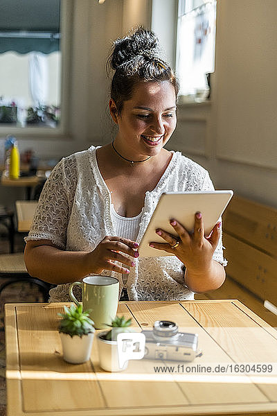 Lächelnde junge Frau  die ein digitales Tablet benutzt  während sie an einem Tisch in einem Café sitzt