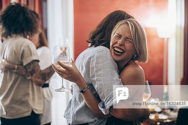 Happy young woman embracing male friend during party at home