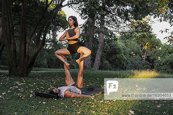 Ein Mann balanciert eine Sportlerin auf den Beinen  während er im Park Acroyoga übt.