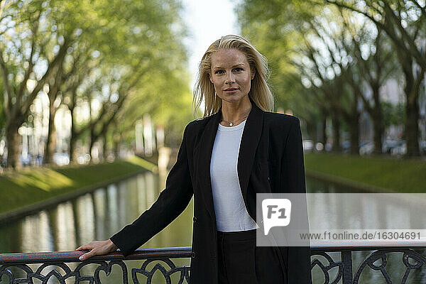 Selbstbewusste blonde Unternehmerin an einem Kanal in der Stadt