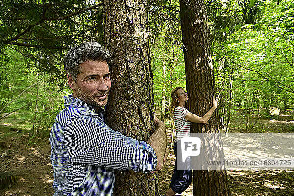 Mann und Frau umarmen einen Baum  während sie im Wald stehen