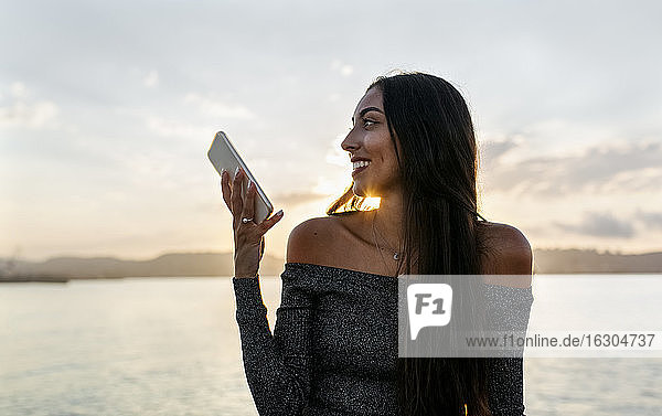 Nachdenkliche Frau  die ein Mobiltelefon gegen den klaren Himmel benutzt