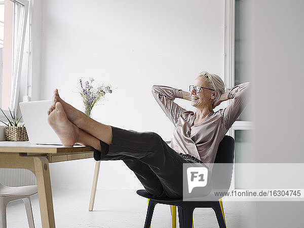 Geschäftsfrau mit Händen hinter dem Kopf entspannt auf einem Stuhl in einem Loft-Büro