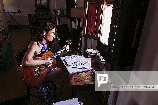 Junge Frau liest Notenblätter  während sie zu Hause Gitarre übt