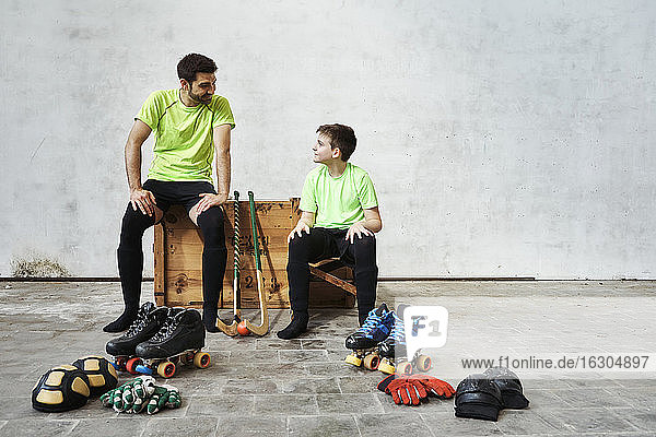Vater und Sohn unterhalten sich  während sie auf einer Holzkiste neben einem Sportgerät an der Wand im Gericht sitzen