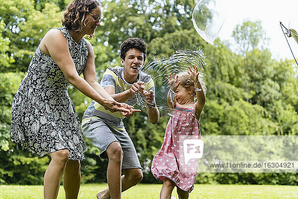 Glückliche Familie beim Platzen einer Seifenblase im Park