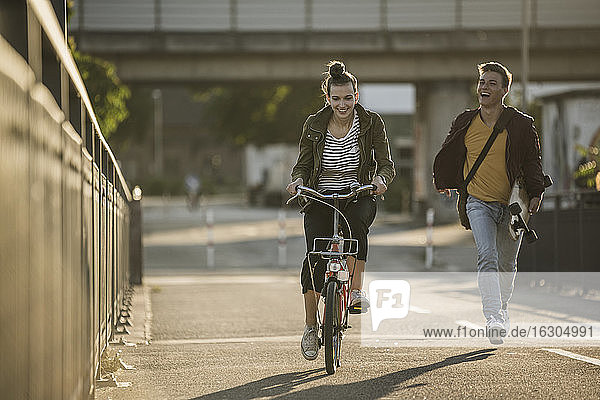 Fröhlicher Freund läuft hinter seiner Freundin auf dem Fahrrad in der Stadt an einem sonnigen Tag