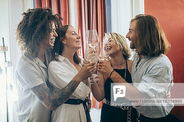Cheerful male and female friends toasting wineglasses during party at home