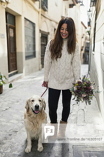 Frau hält Blumenstrauß und steht mit Hund auf der Straße in der Stadt