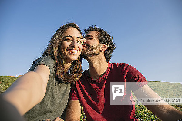 Frau  die ein Selfie mit einem Mann macht  während sie im Gras sitzt