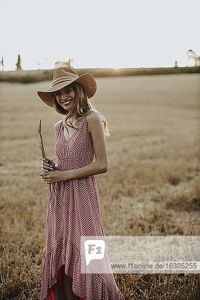 Cheerful young woman standing in wheat field during sunset
