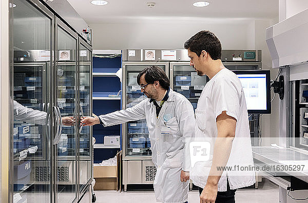Doctor standing with male coworker opening refrigerator in pharmacy