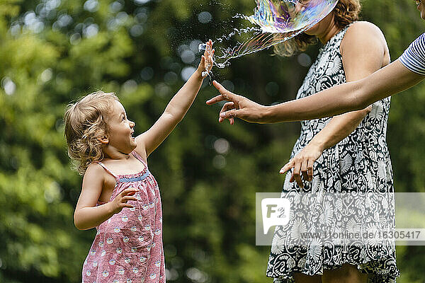 Mädchen lässt beim Spielen mit der Familie im Park eine Seifenblase platzen