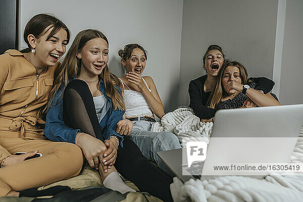 Eine Gruppe von Freundinnen sitzt auf dem Bett und schaut einen Film auf dem Laptop