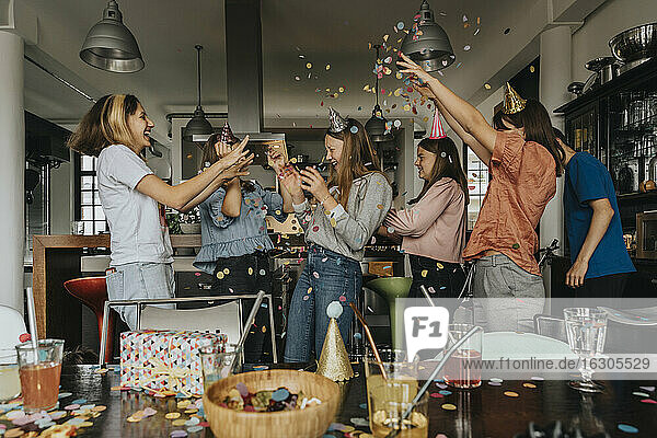 Cheerful friends throwing confetti on birthday girl while celebrating at home