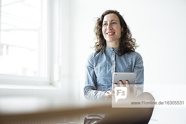 Lächelnde Geschäftsfrau  die ein digitales Tablet benutzt  während sie an der Wand sitzt