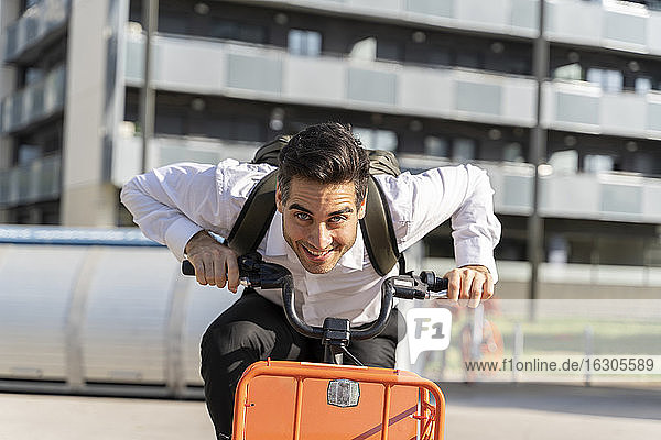 Cheerful male entrepreneur riding electric bicycle against building in city