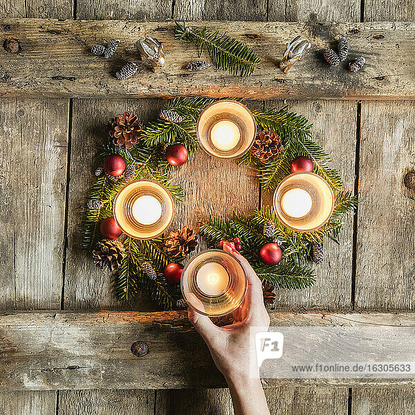 Die Hand einer Frau berührt die Glasabdeckung einer brennenden Kerze auf einem Adventskranz