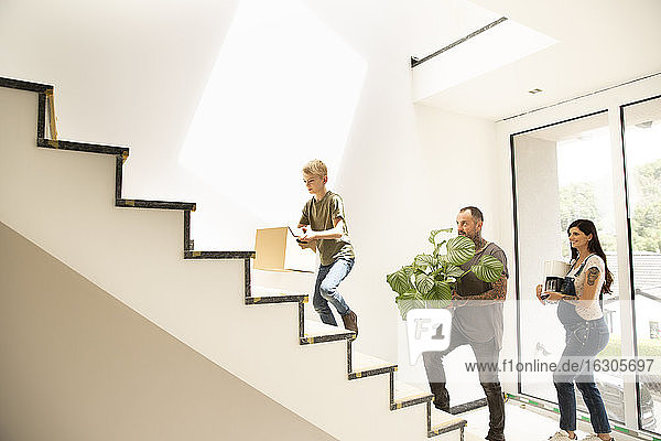 Eine Familie  die verschiedene Gegenstände trägt  während sie in ihrem neuen Haus die Treppe hinaufsteigt