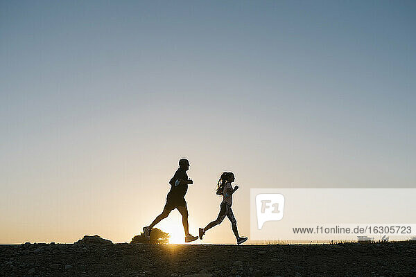 Silhouette of athlete and woman running against clear sky during sunset