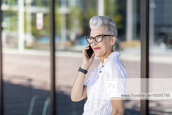 Lächelnde Frau  die mit ihrem Smartphone gegen ein Glasfenster spricht