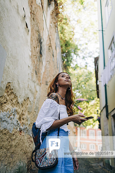 Young woman using phone ehile standing at alley in Alfama  Lisbon  Portugal