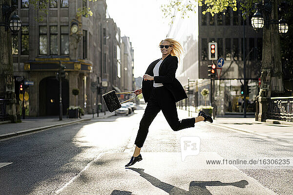 Fröhliche Unternehmerin läuft beim Überqueren der Straße in der Stadt