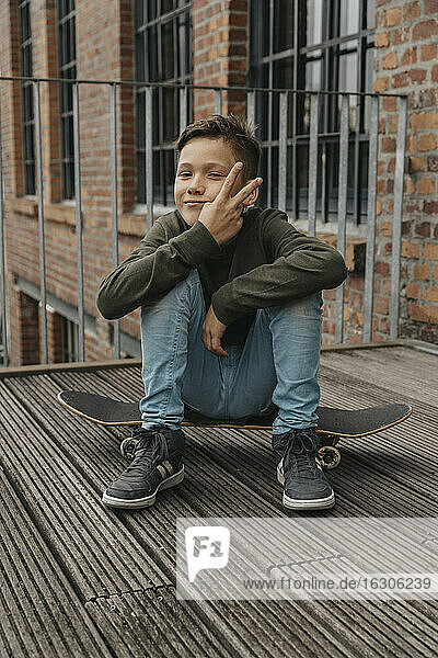 Smiling boy showing peace sign while sitting on skateboard against building
