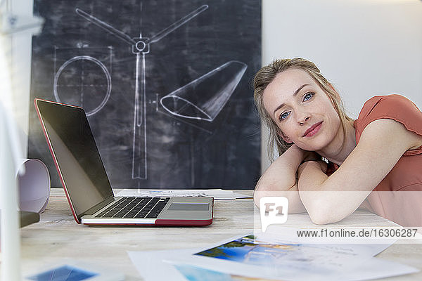 Porträt einer selbstbewussten Frau  die sich im Büro auf den Schreibtisch stützt