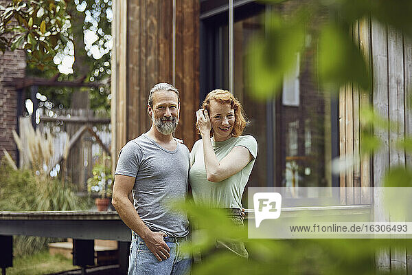 Lächelndes Paar vor einem kleinen Haus im Hof