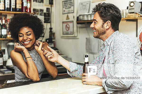 Mann berührt fröhliche Barkeeperin beim Flirten mit ihr am Bartresen