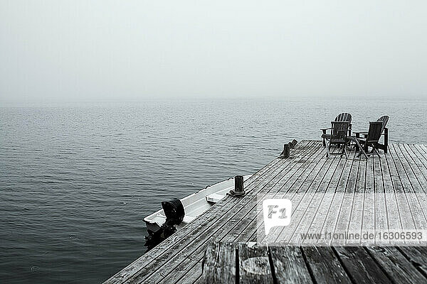Empty deck chairs on coastal jetty at foggy dawn