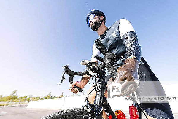 Male cyclist with artificial limb riding bicycle against clear sky during sunny day