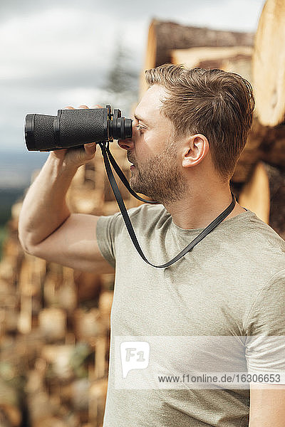 Close-up of male hiker looking through binoculars while standing in forest