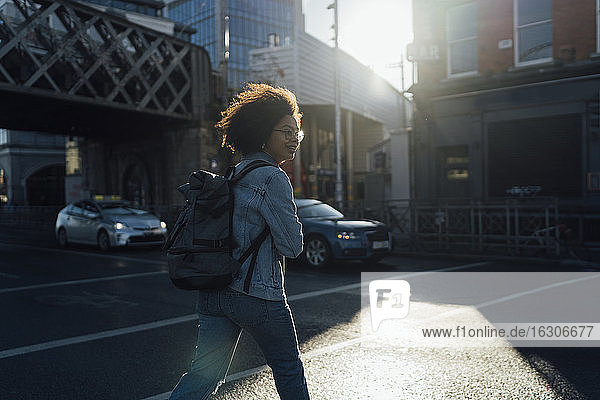 Afro junge Frau mit Rucksack beim Überqueren der Straße in der Stadt