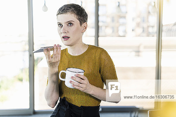 Geschäftsfrau im Büro  die einen Kaffeebecher hält und ein Smartphone benutzt