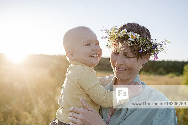 Frau mit Kranz und fröhlichem Sohn in der Hand an einem sonnigen Tag