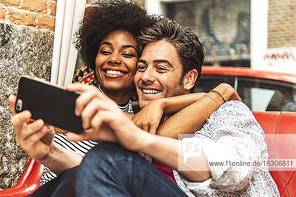 Close-up of happy woman embracing boyfriend taking selfie in cafe