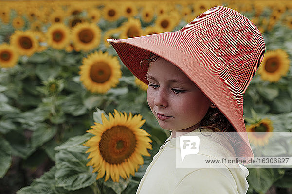 Nettes Mädchen mit Sonnenhut in einem Sonnenblumenfeld im Sommer