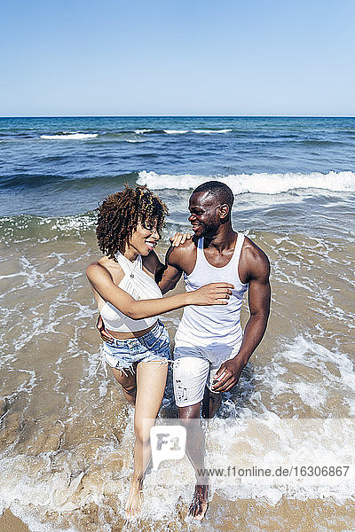 Happy couple walking in sea against clear sky during summer
