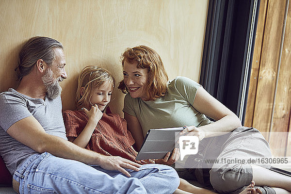 Smiling parents with daughter using digital tablet while relaxing on bed at home