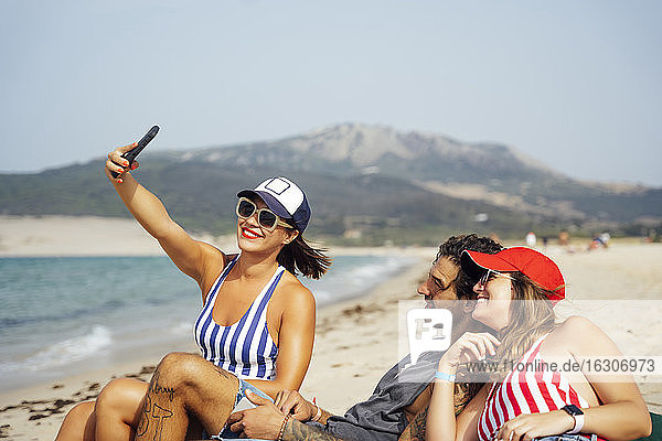 Lächelnde Frau macht Selfie mit männlichen und weiblichen Freunden am Strand  Tarifa  Spanien