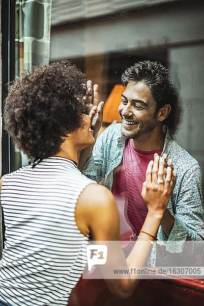 Happy couple looking at each other through window of cafe