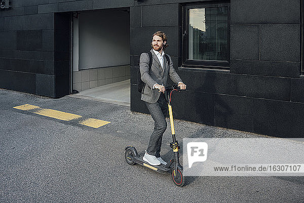 Young businessman riding electric push scooter to commute in city