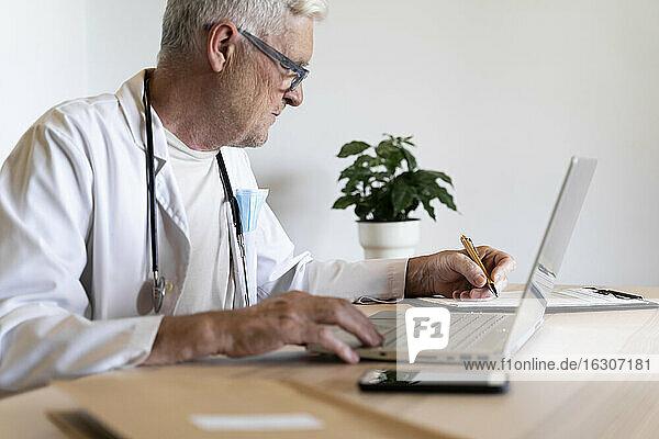 Senior doctor working on laptop while sitting in his clinic