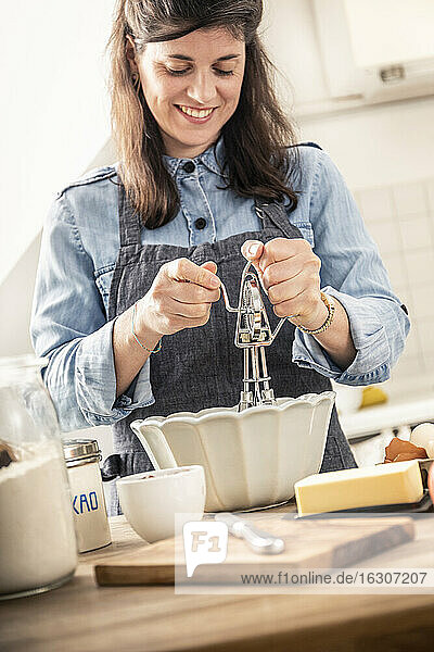 Lächelnde Frau  die einen Schneebesen benutzt  während sie in der Küche zu Hause steht