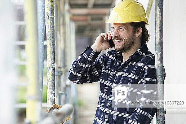 Bauarbeiter  der über sein Smartphone spricht  während er an einem Gerüst auf der Baustelle steht
